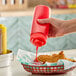 A red 16 oz. wide mouth squeeze bottle being used to dispense sauce onto food.
