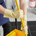 A person wearing Cordova beige latex gloves holding a yellow mop handle.