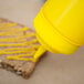 A person using a yellow Choice wide mouth squeeze bottle to put mustard on a piece of bread.