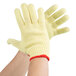 A pair of yellow Cordova Aramid / Cotton work gloves with red trim on a person's hands.