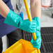 A person in green Cordova Nitrile gloves holding a yellow mop handle.