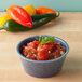 A blue polyethylene ramekin filled with salsa on a table.