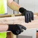 A person wearing Cordova black gloves with nitrile dots holding a piece of wood.