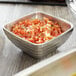 A Vollrath stainless steel bowl of chopped tomatoes and onions on a table.