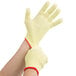 A pair of yellow Cordova work gloves with red trim being worn on a pair of hands.