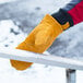 A person wearing a Cordova russet leather freezer mitten holding a metal bar with snow on it.