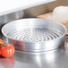 An American Metalcraft Super Perforated Heavy Weight Aluminum Pizza Pan with holes on it next to a ball of dough.