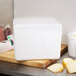 A white Nordic insulated shipping box with a white foam cube inside on a table with cheese and meat on a cutting board.