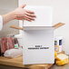 A person opening a Nordic insulated shipping box with a white polystyrene cooler inside.