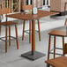 A Lancaster Table & Seating wooden bar height table with a live edge and rustic walnut finish and metal legs.