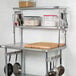 A Regency stainless steel leg mounted pot rack holding utensils and a cutting board over a table.