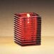 A Sterno red ribbed glass candle holder with a lit candle.