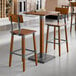 A bar height table set with a square rustic walnut finish wood table and two matching bar stools featuring metal accents.