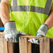 A man wearing Cordova warehouse work gloves and a safety vest holds a piece of wood.