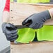 A person wearing Cordova gray warehouse gloves with black sandy nitrile palm coating holding a piece of wood.