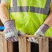 A man wearing Cordova striped canvas warehouse gloves and a safety vest holding a piece of wood.