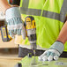 A man in a safety vest using a Cordova green and pink striped work glove to drill holes in metal.