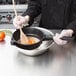 A person using a Matfer Bourgeat medium mesh sieve to sift flour over a bowl of food.