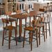 A Lancaster Table & Seating rustic walnut live edge bar height table with chairs around it.