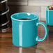 A turquoise Fiesta china mug with a handle filled with coffee on a table.