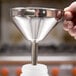 A hand using a Matfer Bourgeat stainless steel funnel to pour liquid into a plastic container.