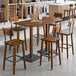 A Lancaster Table & Seating bar height table with a rustic walnut finish and metal legs with bar stools.