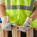 A man wearing Cordova Tuf-Cor white canvas work gloves with heavy side split leather palm coating and rubber cuffs and a safety vest.