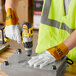 A person wearing Cordova leather welding gloves and a safety vest using a drill to make a hole in a metal box.