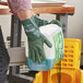 A person wearing a green Cordova ActivGrip glove pouring cleaning liquid into a container.