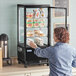 A woman taking food from an Avantco countertop display refrigerator with glass sides.