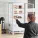 A woman standing in front of a white Avantco countertop display refrigerator with glass sides.