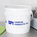 A white bucket with blue text labeled "Campus Products Inc" filled with green vegetable granulate.