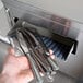 A hand holding a pile of silverware in a metal container being dried and polished by a Campus Products Countertop Cutlery Dryer.