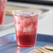 A clear compostable plastic cold cup filled with a red iced beverage.