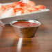 A Carlisle stainless steel round sauce cup filled with red sauce next to a plate of shrimp.