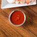 A Carlisle stainless steel sauce cup filled with red sauce next to a plate of shrimp.