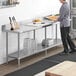 A man standing at a Regency stainless steel work table in a kitchen.