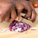 A person using a Town onion knife to cut a red onion on a cutting board.