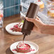 A brown 12 oz. wide mouth squeeze bottle being used to drizzle sauce on a dessert.
