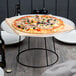 An Acopa black metal display stand with a pizza on a plate.