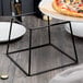 A plate of pizza on a black metal Acopa display stand.