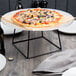An Acopa black metal display stand holding a pizza on a table.