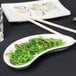 A Tuxton porcelain white crescent dish with green seaweed on a table.