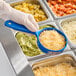 A person using a Carlisle blue 8 oz. measuring spoon to serve shredded cheese.
