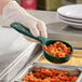 A person in gloves holding a Carlisle green perforated spoon of food over a food tray.