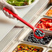 A person using a Carlisle red long handle portion spoon to serve blueberries from a tray.