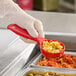 A gloved hand using a Carlisle red plastic short handle perforated portion spoon to serve food.