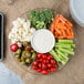 A Fineline clear plastic 7-compartment tray with vegetables and dip, including a bowl of ranch, broccoli, and baby carrots.