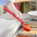 A person holding a Carlisle red perforated portion spoon over a food container.