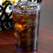 A Cambro slate blue plastic tumbler filled with ice and brown liquid on a table.